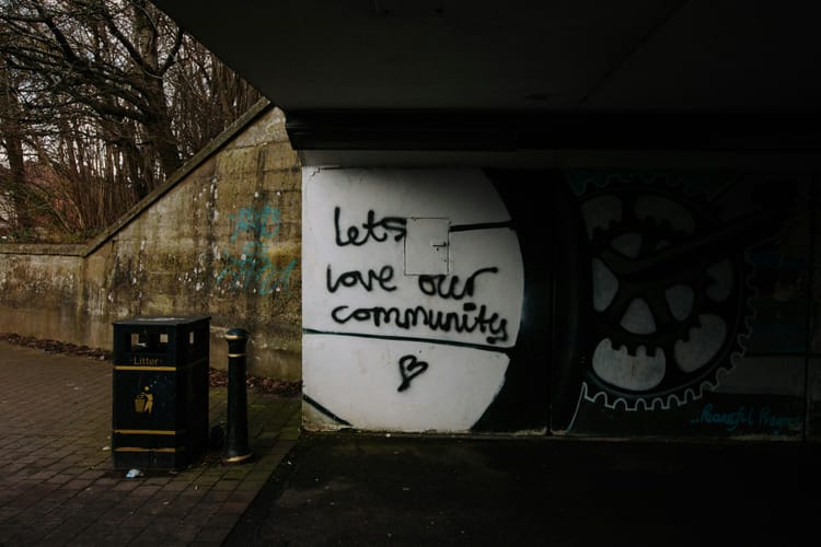 pedestrian bridge underpass with black graffiti on white background reading LET'S LOVE OUR COMMUNITY